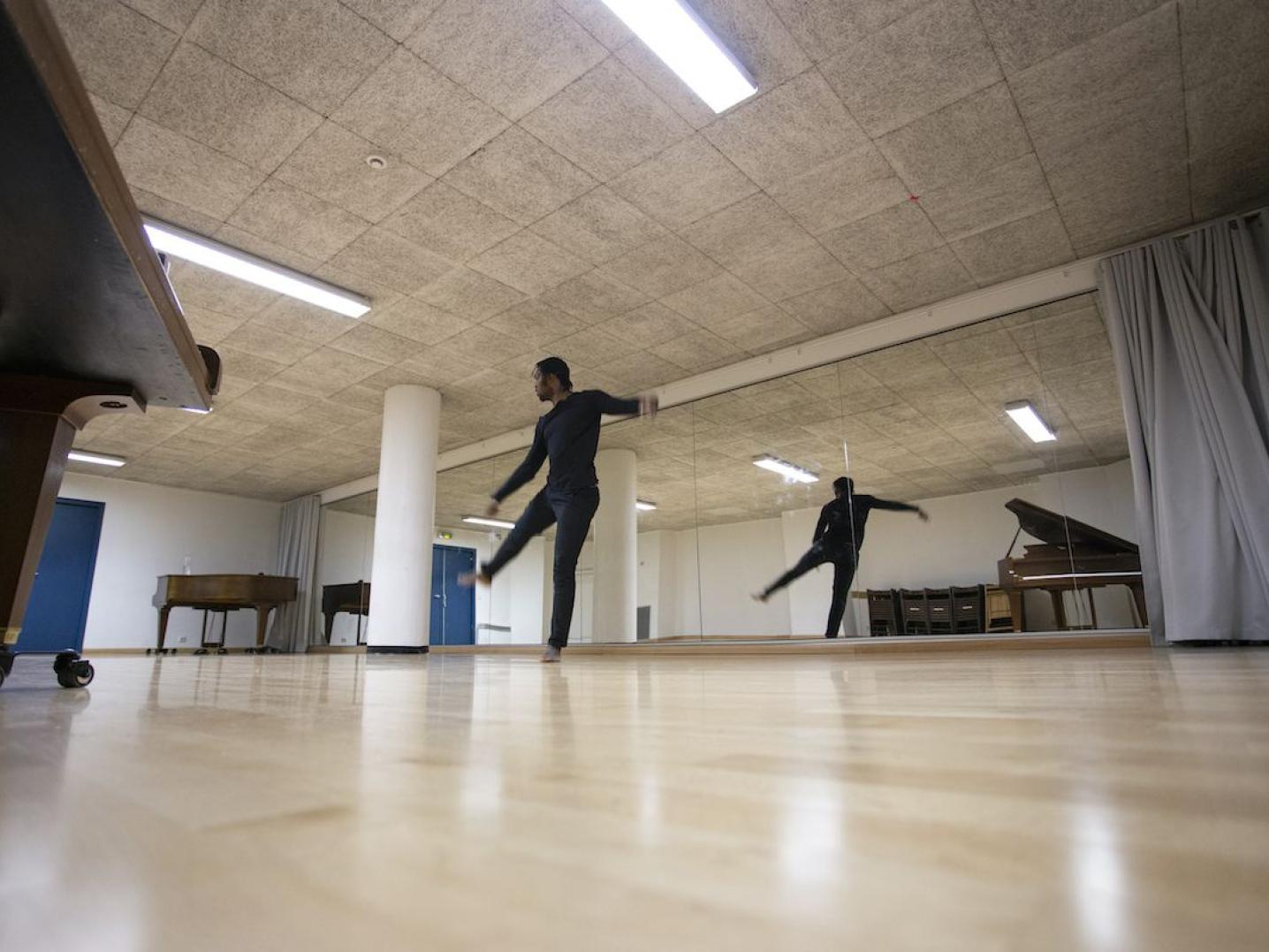 a dance rehearsal studio where a man is dancing and his image is reflected in a large mirror on the wall
