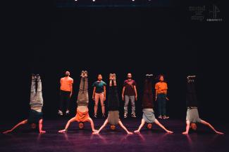 A group of dancers on a stage standing in two rows, the first row of people is standing on their heads, the back row is standing upright.