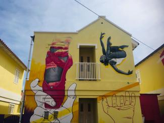 A building on Curaçao with yellow walls and a large painting of a ballet shoe and dancers