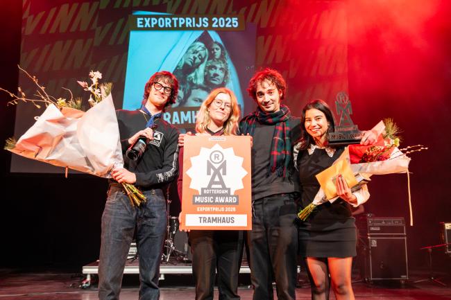 four broadly smiling people on a stage with bouquest of flowers and an award in their hands