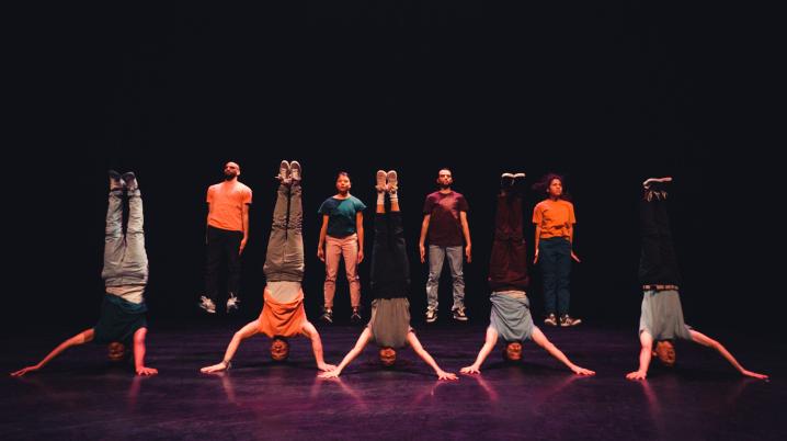 A group of dancers on a stage standing in two rows, the first row of people is standing on their heads, the back row is standing upright.