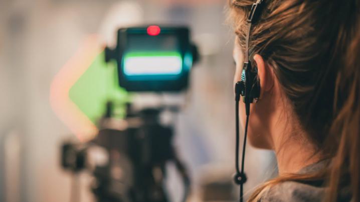 A female film professional stands behind a film camera