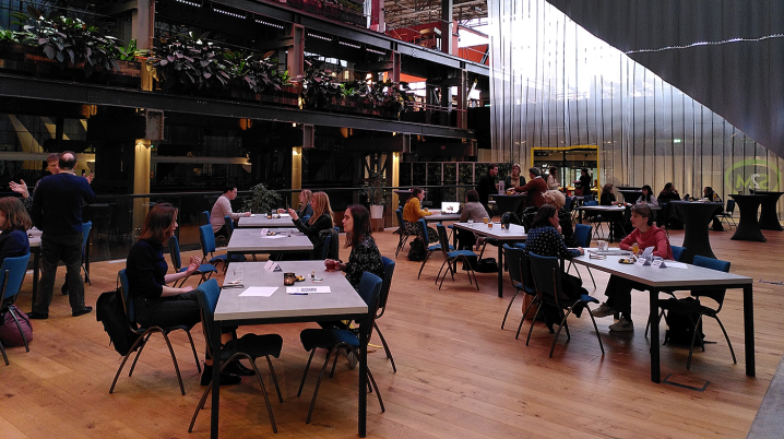A group of people sitting around multiple tables in a large hall