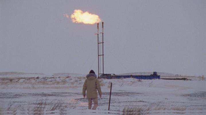 Man in the snow, walking up to an oil pipeline