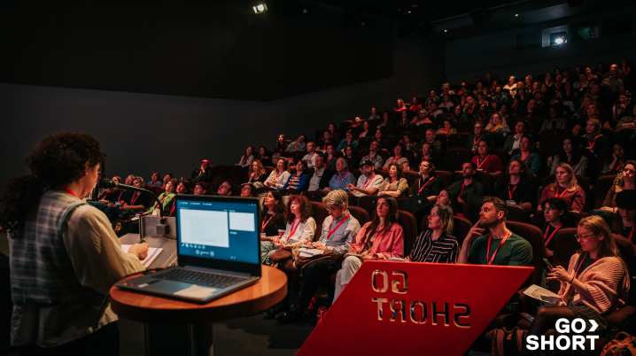 auditorium filled with people sitting on read chairs and wearing red key cords