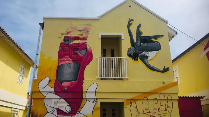 A building on Curaçao with yellow walls and a large painting of a ballet shoe and dancers